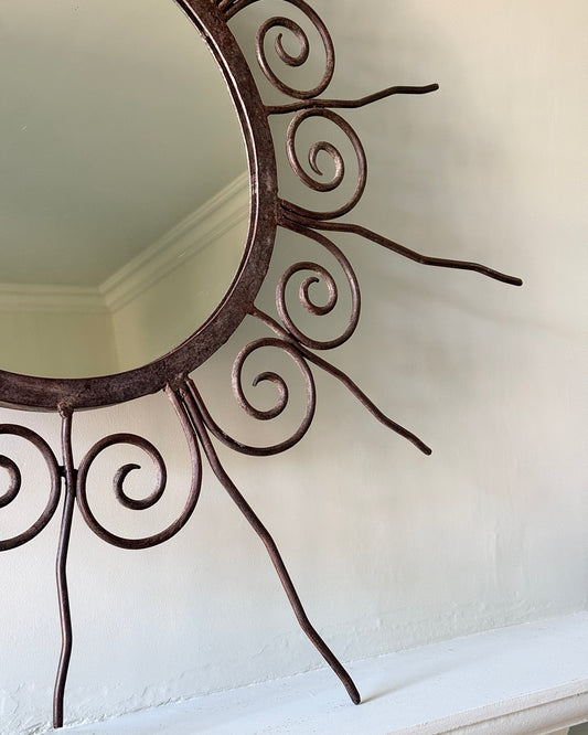 A round wrought rustic black iron sunburst shape mirror with wavy graduating rays. French, circa, 1950's. This mirror would be perfect in a hallway, bedroom or living area.