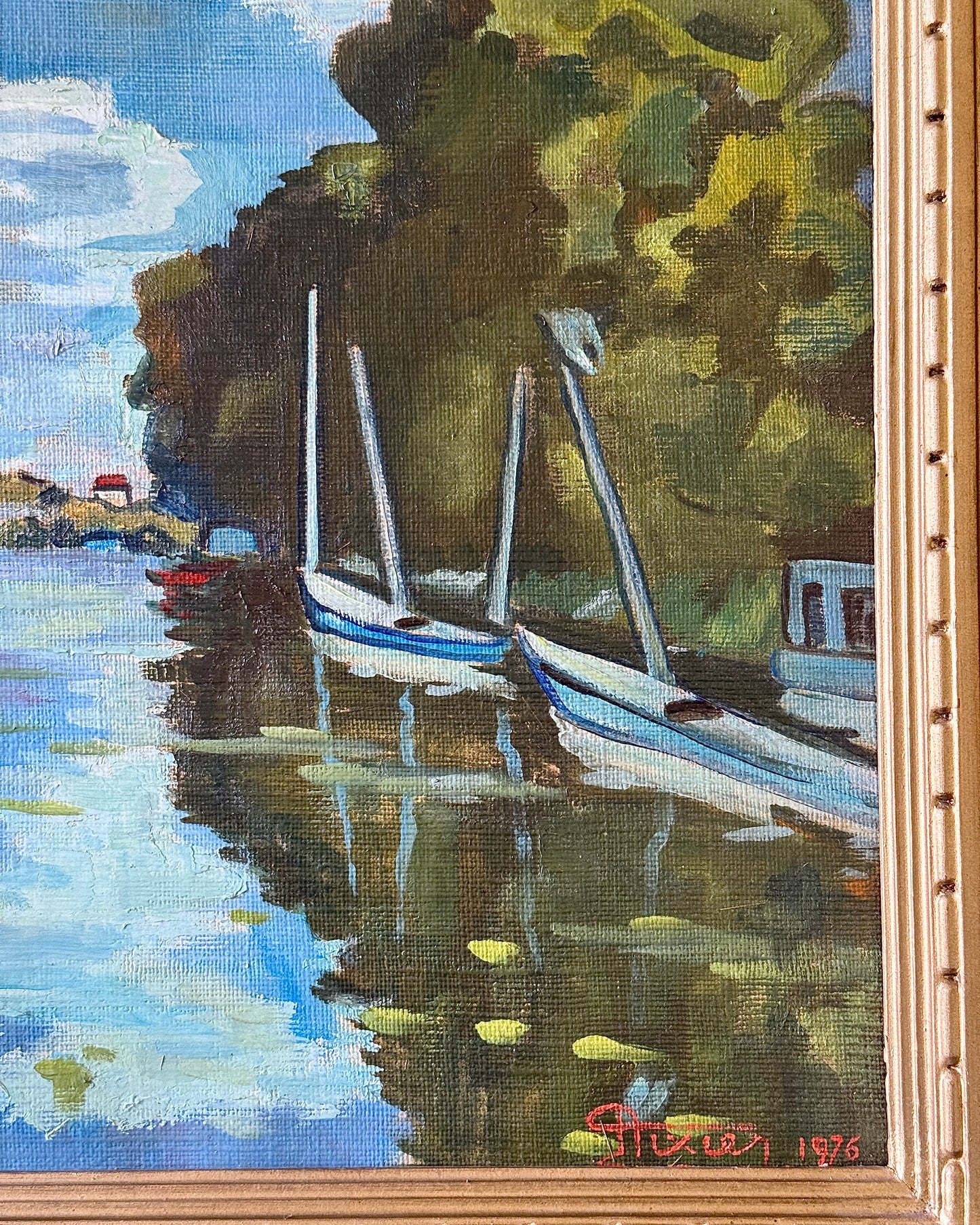 Framed oil on canvas depicting boats on the river Seine in Poissy, near Paris. Attributed to the style of Albert Marquet, a French painter. Signed Axier 1976. An impressionist painting with the use of bright blue and white colours used throughout the landscape, with small trees dotting the shoreline and fluffy clouds in a pale sky above.