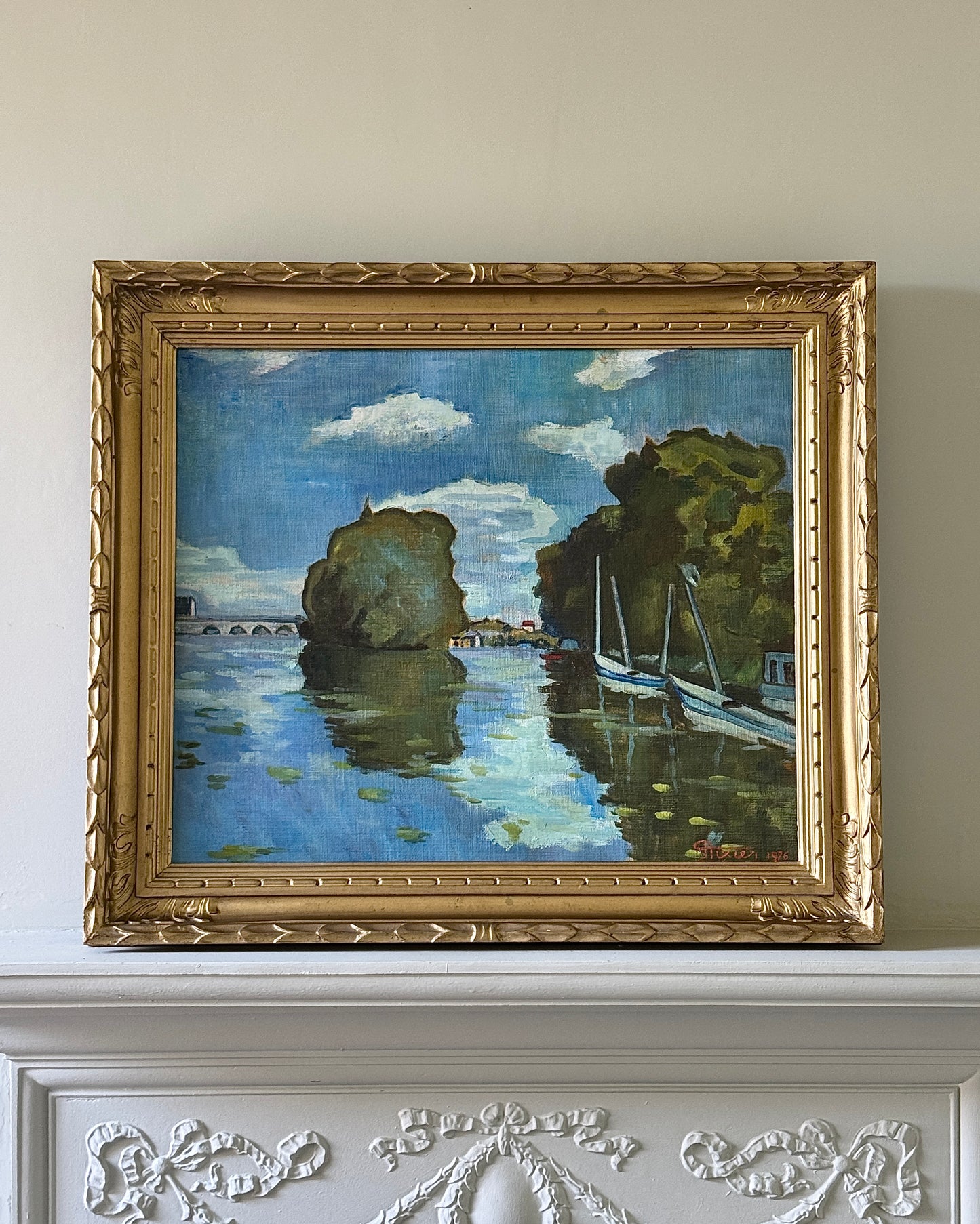 Framed oil on canvas depicting boats on the river Seine in Poissy, near Paris. Attributed to the style of Albert Marquet, a French painter. Signed Axier 1976. An impressionist painting with the use of bright blue and white colours used throughout the landscape, with small trees dotting the shoreline and fluffy clouds in a pale sky above.