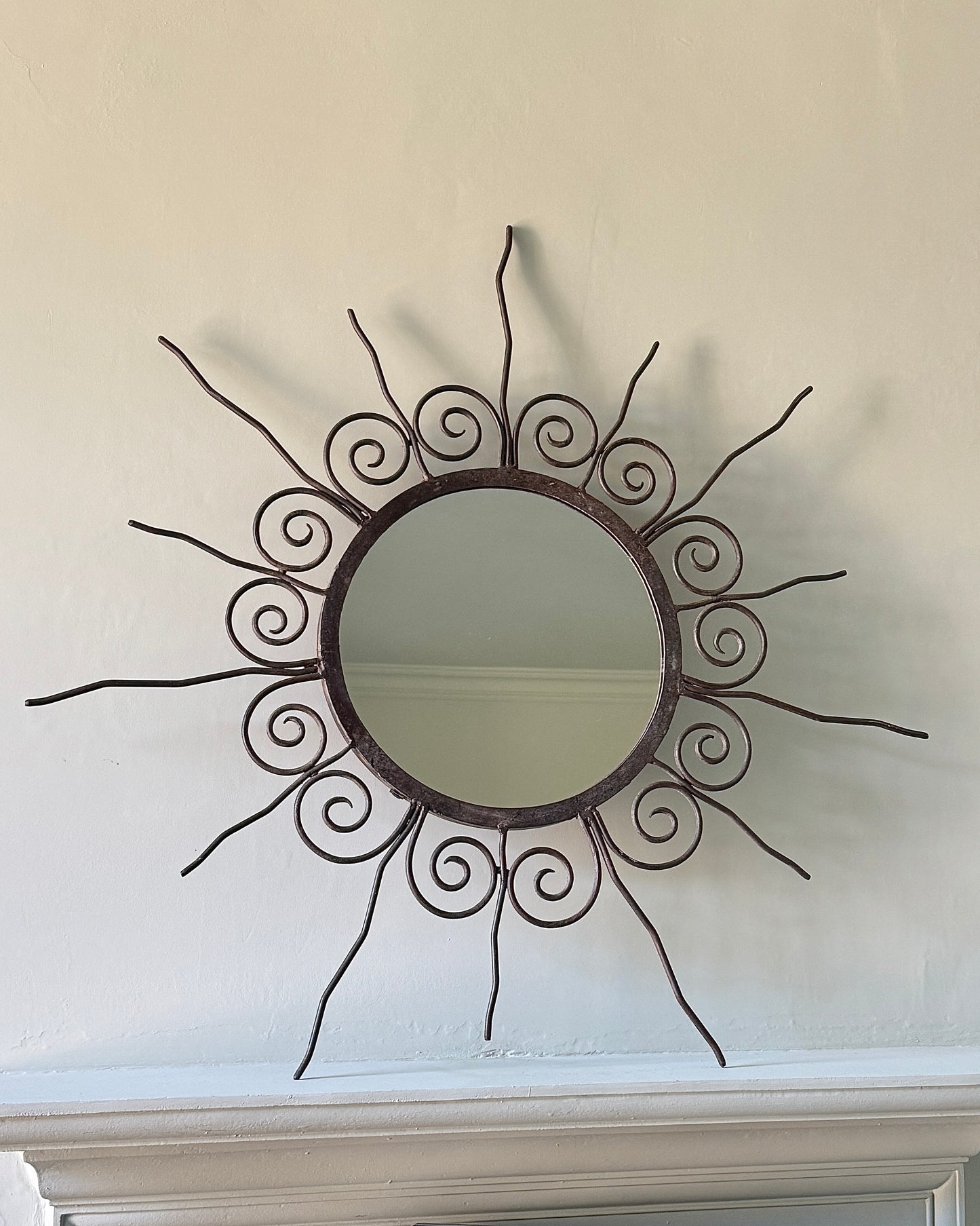 A round frenchwrought rustic black iron sunburst shape mirror with wavy graduating rays and swirl details. French, circa, 1950's. This mirror would be perfect in a hallway, bedroom or living area.