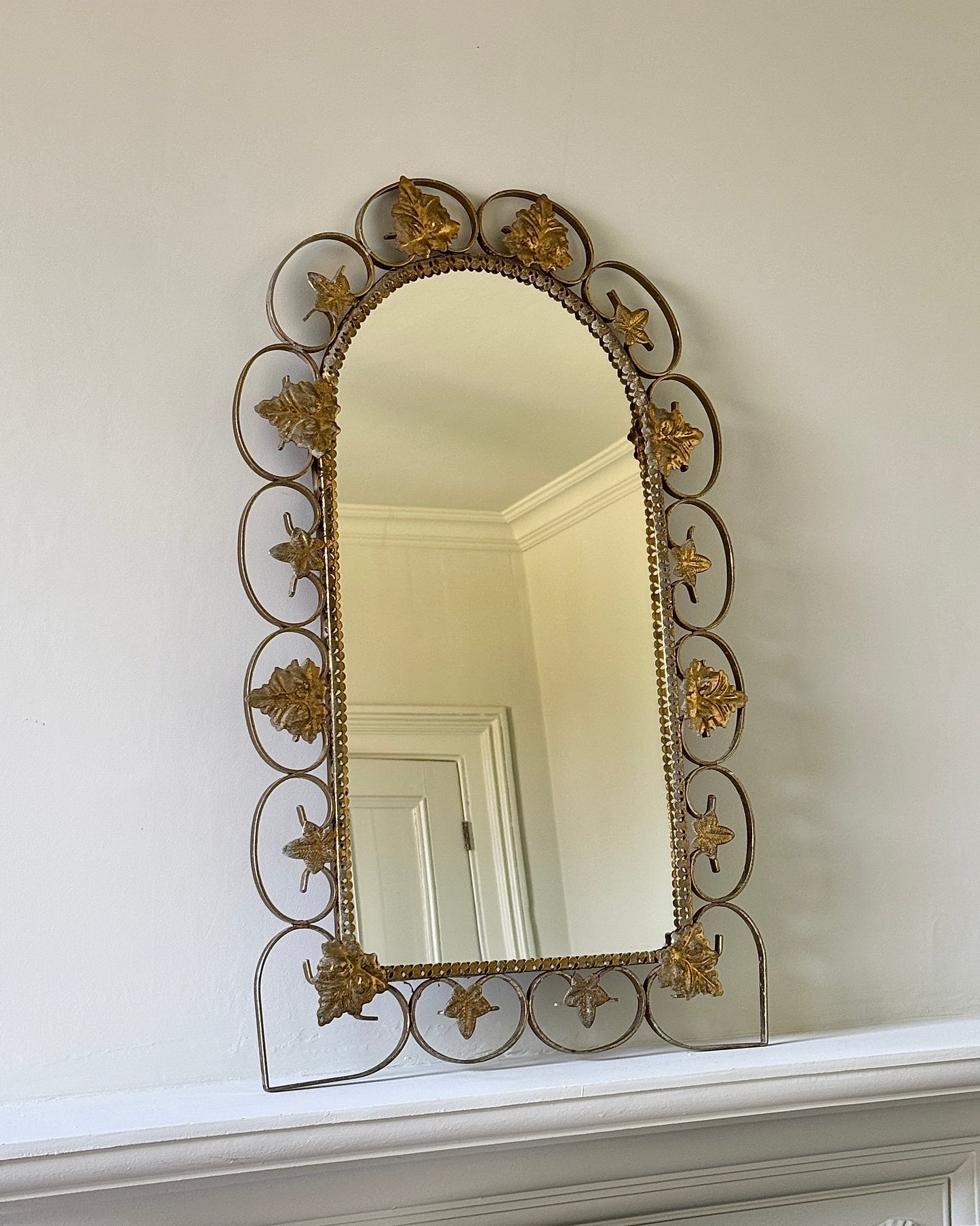 A mid century arched mirror, with a brass metal scroll frame in the shape of flowers, leaves and swirls which give an ultra delicate, feminine finish.